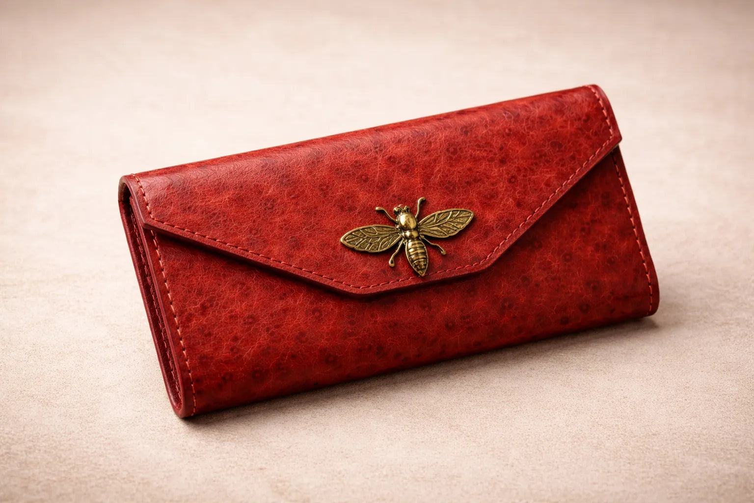 Lähikuva Toe-Nahka Designin punaisesta, tekstuuripintaisesta nahkalompakosta, jossa on koristeellinen kullanvärinen mehiläissolki.