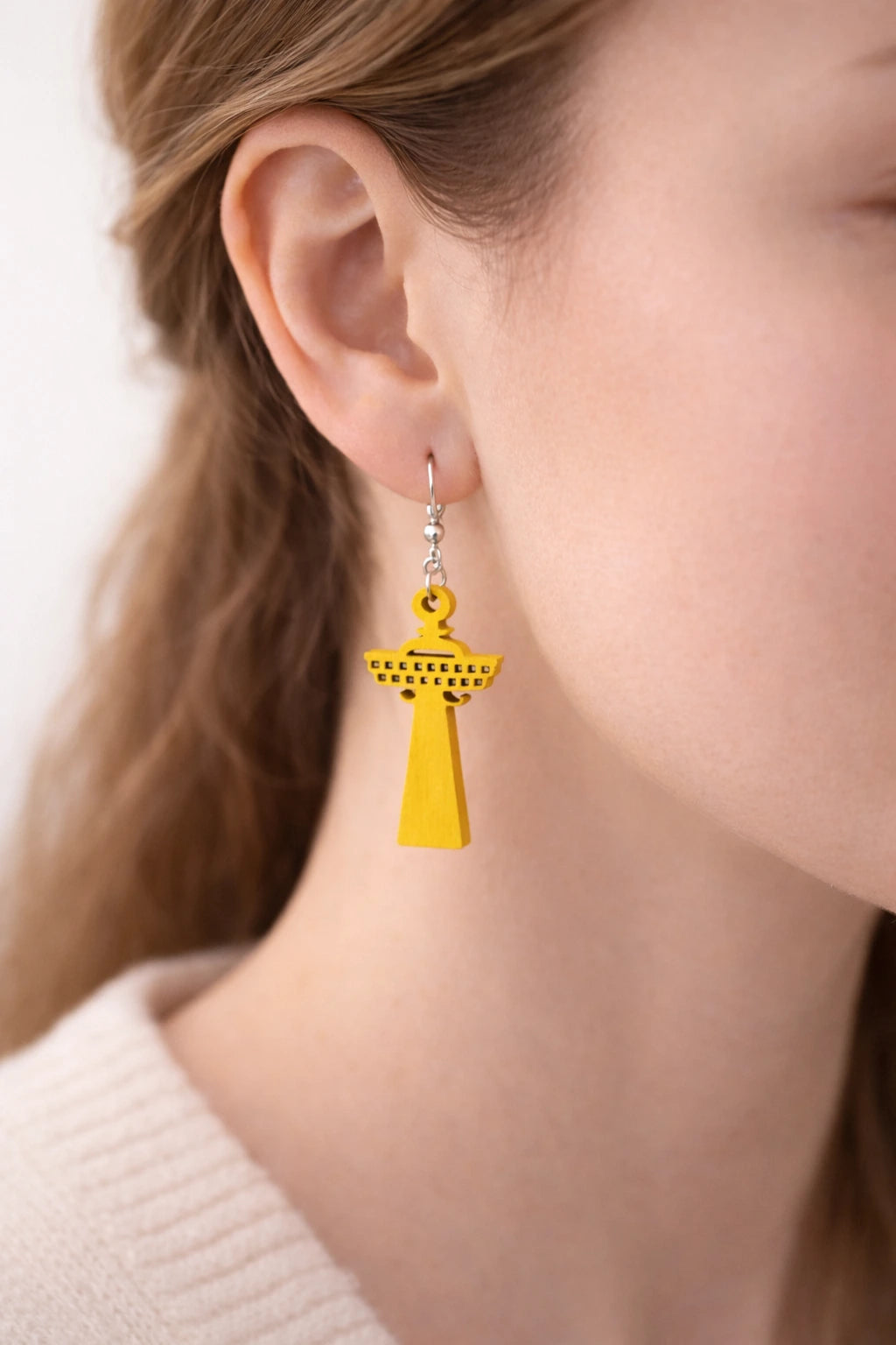 Lähikuva mallin korvassa olevasta keltaisesta, puisesta Näsinneula-korvakorusta – korostaa laserleikatun koivuvanerin tarkkoja yksityiskohtia ja raikkaan keltaista sävyä.