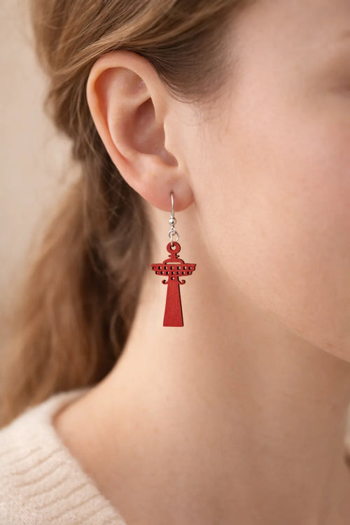 Lähikuva mallin korvassa olevasta punaisesta, puisesta Näsinneula-korvakorusta – korostaa laserleikatun koivuvanerin tarkkoja yksityiskohtia ja syvää punaista sävyä.