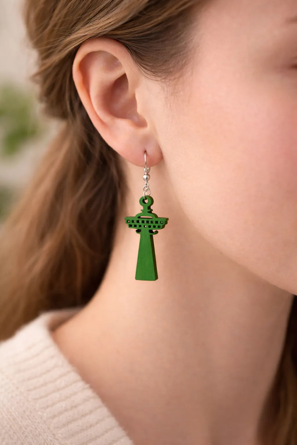 Lähikuva mallin korvassa olevasta vihreästä, puisesta Näsinneula-korvakorusta – korostaa laserleikatun koivuvanerin tarkkoja yksityiskohtia ja raikkaan vihreää sävyä.