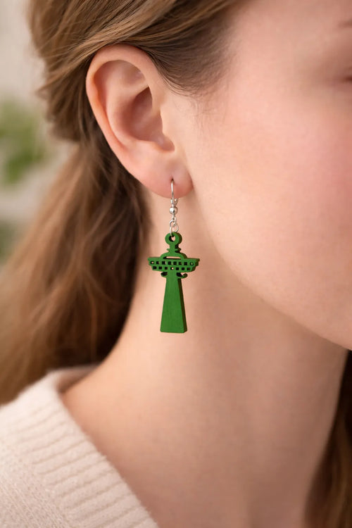 Lähikuva mallin korvassa olevasta vihreästä, puisesta Näsinneula-korvakorusta – korostaa laserleikatun koivuvanerin tarkkoja yksityiskohtia ja raikkaan vihreää sävyä.